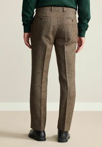Tweed trousers in brown with a textured finish, featuring a straight cut, two back pockets, and black shoes.