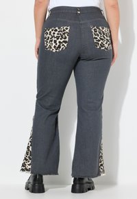 Pantalones de mezclilla acampanados en gris oscuro con bolsillos y paneles laterales de estampado de leopardo, acabados con bordes sin rematar y zapatos de plataforma negros.