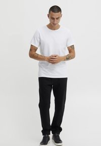 Camiseta de algodón blanca con cuello redondo, combinada con pantalones de chándal negros con puños elásticos y zapatillas negras de diseño minimalista.