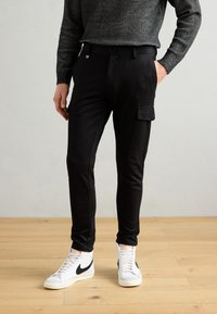 Sorte cargo bukser med slim fit, med en sidelomme, glat stoftekstur, og parret med hvide høj-toppede sneakers.