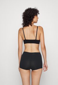 Black bra and high-waisted shorts, both made of ribbed fabric. Features thin straps and a seamless design, with a smooth texture.