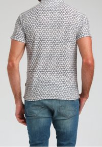 Kortärmad t-shirt i ljusgrått med ett geometriskt triangelmönster i mörkgrått. Mjuk tyg, rund hals och rak fåll. Bärs med blå jeans.