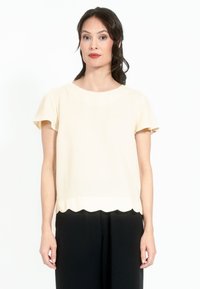 Lühikeste varrukatega kreemivärvi bluus, millel on laineline äär ja sile tekstuur, koos mustade pükstega. Lihtne ümar dekoltee ja mugav lõige.