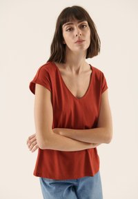 Rust-colored short-sleeve t-shirt with a V-neck, featuring soft fabric and a relaxed fit. Paired with light blue denim jeans.