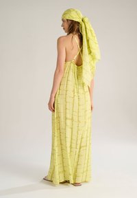 Abito maxi in tessuto giallo leggero e semi-trasparente con un motivo verticale; presenta spalline regolabili e un foulard abbinato.