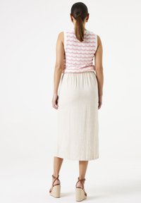 Robe en lin avec une taille froncée ; le haut sans manches présente un motif de vagues roses ; couleur naturelle pour la jupe, associée à des sandales compensées à lanières.