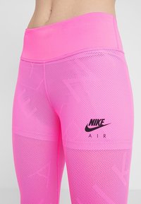 Jasnoróżowe legginsy Nike Air z wysokim stanem i teksturą z siateczki, noszone na dolnej części tułowia i górnej części nóg.