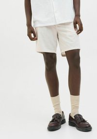 Pantalones cortos de un tono beige claro, fabricados en un tejido texturizado, combinados con calcetines crema y zapatos de cuero marrón con un fleco decorativo.