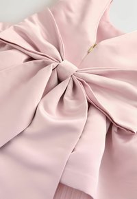 Gaiši rozā kleita ar lielu loku jostas daļā, izgatavota no maigas, gludas auduma un ar paslēptu rāvējslēdzēju ar zelta aksesuāriem.