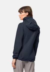 Veste marine foncée résistante à l'eau avec capuche, poignets élastiques et une discrète étiquette logo en bas. Texture lisse ; design léger.