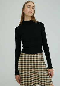 Schwarz gestreifte Langarmoberteil mit gewelltem Saum, kombiniert mit einem karierter Rock in Braun-, Beige- und Schwarztönen im knielangen Design.