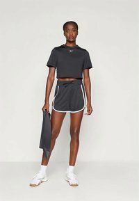 Μαύρο κοντό μπλουζάκι και ταιριαστά σορτς με λευκή τρέσα, ελαφρύ ύφασμα, μέση με κορδονάκι, και μοντέλο που κρατάει ένα γκρι αντικείμενο.