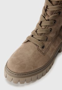 Bottine en suédine marron avec un bout rond, un laçage à plat, une épaisse semelle en caoutchouc avec des crampons prononcés, et des œillets en métal.