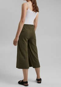 Pantaloni verdi a gamba larga realizzati in tessuto testurizzato con vita elasticizzata e lunghezza cropped, abbinati a sandali neri.