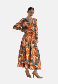 Robe maxi en tissu orange avec des feuilles vertes et des accents crème, décolleté en V, manches longues et taille liée. Texture douce, motif floral.