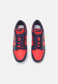 Nike-sneakers med en röd och marinblå läderöverdel, rund tå, perforerade detaljer, tjocka marinblå snören och en vit gummisula.