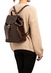 Zaino in pelle marrone con chiusura a cordoncino, due tasche laterali con zip e spallacci regolabili. Texture liscia con una finitura lucida.
