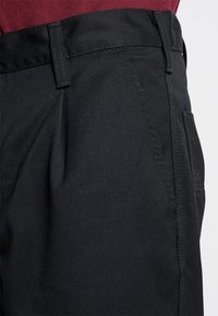 Pantalones negros de tejido entrelazado con una textura suave, que presentan un corte recto, bolsillos laterales y un asa en la cintura.