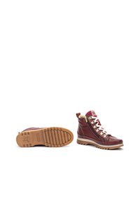 Bottes de randonnée en cuir bordeaux avec une surface texturée, semelle en caoutchouc beige, lacets blancs, éléments en or et fermeture éclair sur le côté pour un enfilage facile.