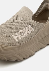 Béžové slip-on tenisky s texturovaným pleteným svrškem, silnou polstrovanou podešví a vyšívaným logem. Gumová podešev má vzor pro lepší trakci.