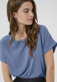 Laisvo kirpimo trumpas rankovėmis viršus, pagamintas iš minkštos mėlynos medžiagos. Turi apvalų iškirpimą ir suktas rankoves. Lygus audinys su minimaliu matomu siūlių skaičiumi.