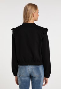Felpa nera con spalle arricciate, vita elastica e maniche lunghe, abbinata a jeans chiari strappati. Tessuto liscio.