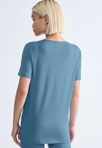 Jasnoniebieska, krótko rękawowa koszulka z miękkiego, gładkiego materiału z okrągłym dekoltem i luźnym krojem, pokazana od tyłu.