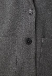 Tmavě šedý vlněný kabát s dvěma černými knoflíky a dvěma předními kapsami, zobrazení detailního texturování a švů.