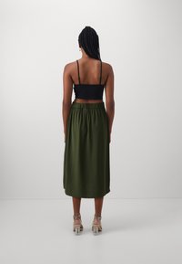 Černý crop top a dlouhá sukně olivové barvy s elastickým pasem. Oblečení doplňují průhledné páskové lodičky. Celkově hladká textura.