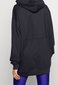 Hoodie nero con una vestibilità rilassata, maniche lunghe e cappuccio. Tessuto morbido e dettagli a pannello cuciti sul retro.