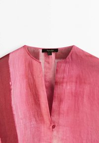 Blouse rose avec une coupe ample, décolleté en V et une fermeture à un seul bouton. Confectionnée en tissu léger avec une texture en dégradé subtil.
