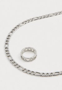 Colar de corrente em prata com elos entrelaçados e um anel texturizado com recortes. Ambos os itens apresentam um acabamento metálico elegante.