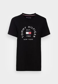 Camiseta de algodón negra con un logo circular que presenta el texto "TOMMY HILFIGER", acentos en rojo y blanco, "EST. 1985" y "NUEVA YORK" debajo.