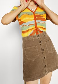 Cardigan lavorato a maglia con motivi a righe gialle, verdi e arancioni, abbinato a una gonna in corduroy marrone con bottoni e tasche.