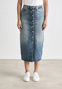 Jeans midi-kjol i ljus till mörkblå gradation, med knäppning fram, bäljear och bakfickor. Matchad med vita sneakers.