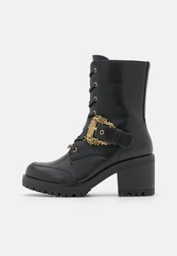 Stivaletto nero realizzato in materiale similpelle, con hardware dorato, stringata frontale, fibbia laterale e tacco chunky con suola strutturata.
