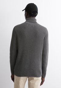 Grauer ribbeliger Pullover mit hohem Kragen, langen Ärmeln und lockerer Passform. Bemerkenswerte Textur und dezentes Designdetail an den Schulternähten.
