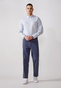 Lichtblauw overhemd met een puntkraag, gecombineerd met donkerblauwe broek en witte sneakers. De stof is glad en zonder patroon.