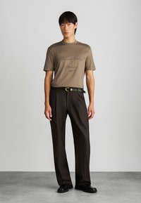 Rudas trumpas rankovėmis marškinėliai su subtiliu grafiniais, derinami su tamsiai rudomis kelnėmis ir juodu diržu su auksine sagtimi. Juodi batai.