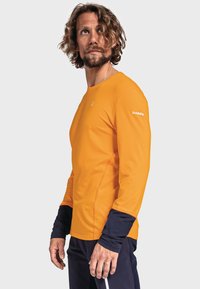 Orange långärmad skjorta med ton-i-ton sömmar, kontrasterande mörkblå manschetter och logodetalj på ärmen. Slät, figurnära tyg.