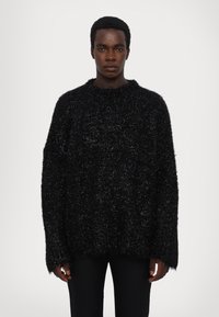 Pulover negru din tricot pufos, cu guler rotund și mâneci lungi supradimensionate. Prezintă un finisaj texturat și o croială lejeră, asociat cu pantaloni negri strâmți.