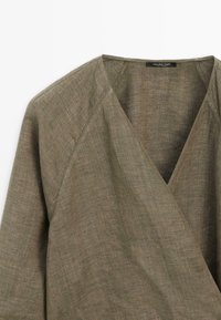 Lniany top na zakładkę w oliwkowym kolorze z długimi rękawami i dekoltem w serek, z widocznymi szwami oraz metką Massimo Dutti na wewnętrznej stronie dekoltu.