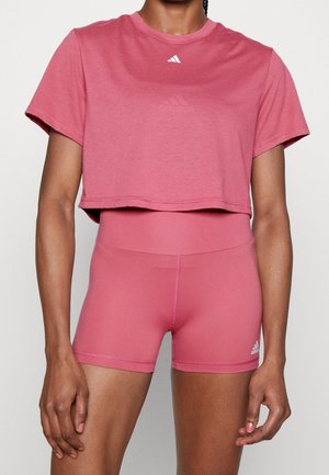 Personne portant un t-shirt court rose assorti et un short de sport taille haute avec des logos Adidas.