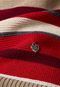 Strickstoff mit roten, cremefarbenen und grauen Streifen, versehen mit einer silbernen Herzmarke, auf der "mit Liebe gemacht" steht. Weiche Textur, gemütliches Aussehen.