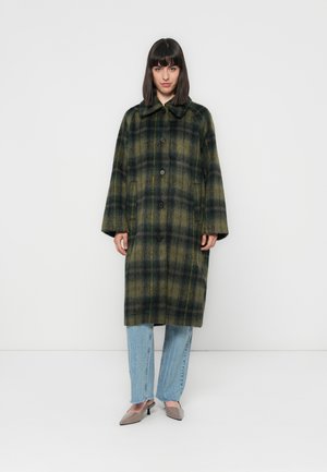 Groen en geel geruite wollen jas met een kraag, oversized pasvorm en knoopsluiting. Draag het over lichtblauwe versleten jeans en beige hakken.