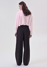 Blusa rosa chiaro con vestibilità ampia e maniche lunghe. Pantaloni neri a gamba larga con vita alta. Texture lisce e design minimal.