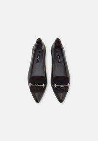 Zapatos planos negros con puntera puntiaguda, que presentan un panel frontal de ante y un hardware decorativo plateado en la parte superior. Textura de cuero suave.