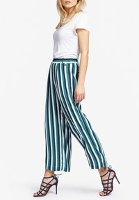 Gestreepte wijde broek in teal, marineblauw en wit, met een elastische tailleband en een losse pasvorm, gecombineerd met strappy marineblauwe hakken.