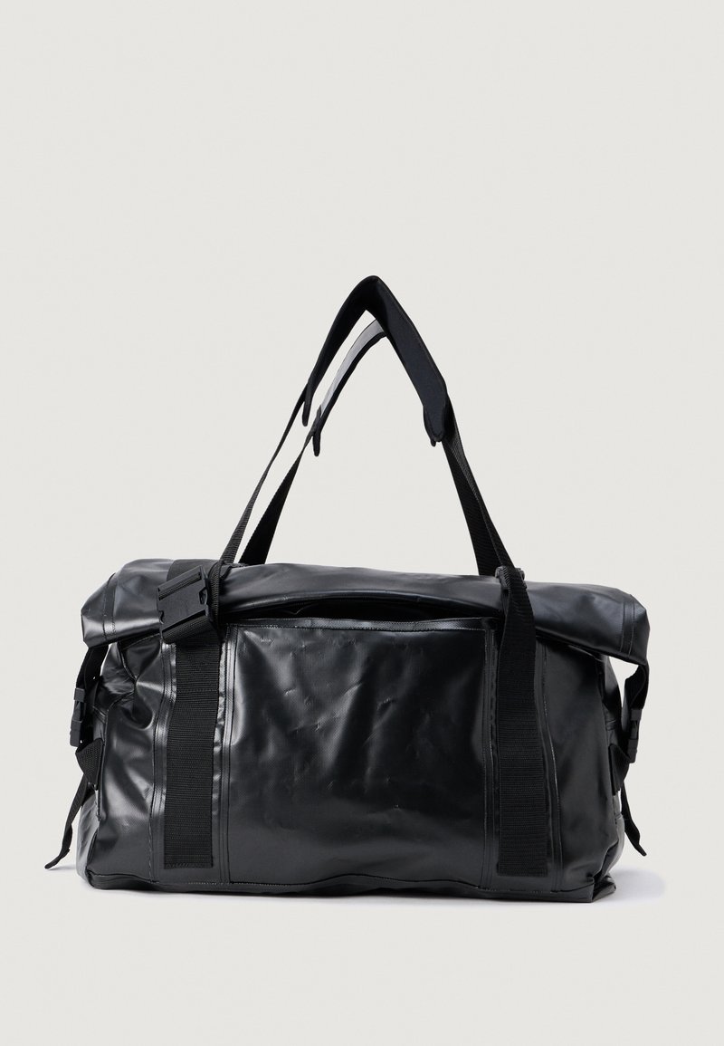 Saco duffel preto feito de material suave e durável, com uma alça ajustável, fivelas laterais e um bolso com zíper na parte superior.