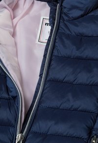 Doudoune marine avec un motif matelassé, fermeture éclair argentée et doublure rose. Étiquette intérieure visible sur le côté gauche. Texture lisse.